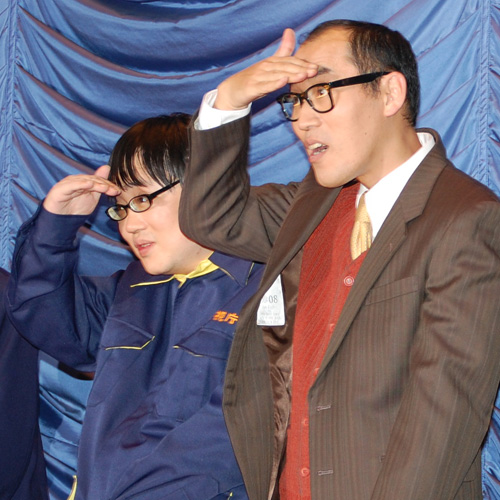 客席で手を挙げている人を探す六角精児（左）と山西惇（右）