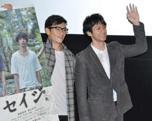 ポスターを片手で持って撮影に応じる伊勢谷友介監督（左）と、手を振る西島秀俊（右）