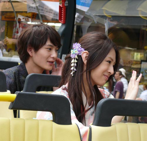 バスの中から道行く人々に手を振る北川景子(右）と岡田将生（左）