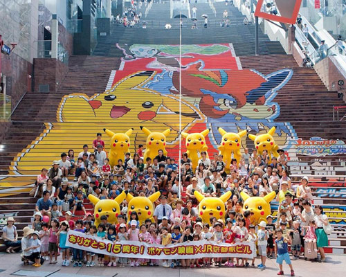 京都駅ビルの大階段に掲出された巨大ポケモンステップアートの前で、9体のピカチュウと中川翔子らが記念撮影